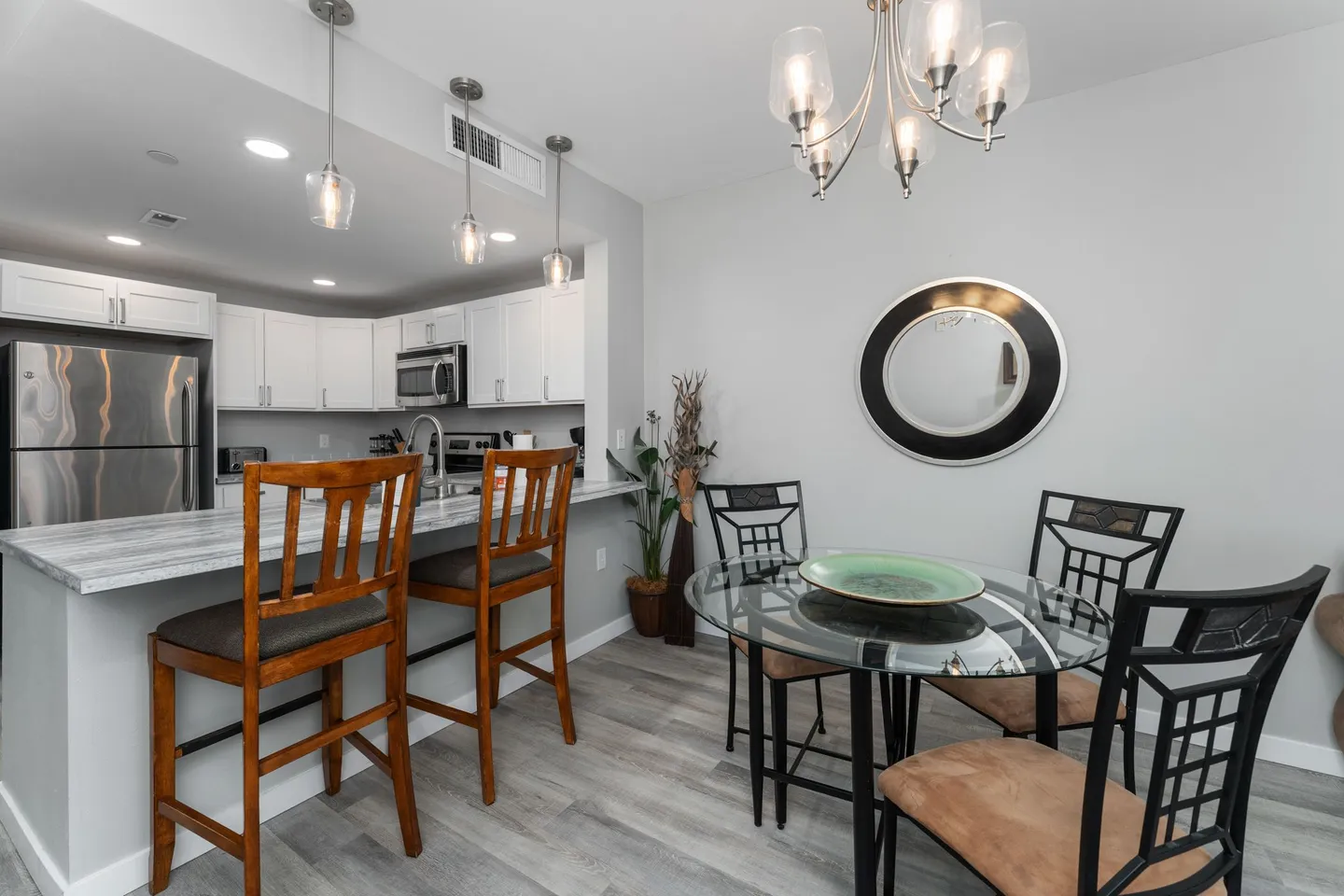 Dining area with a round glass table, pendant lighting, and a breakfast bar overlooking the kitchen.