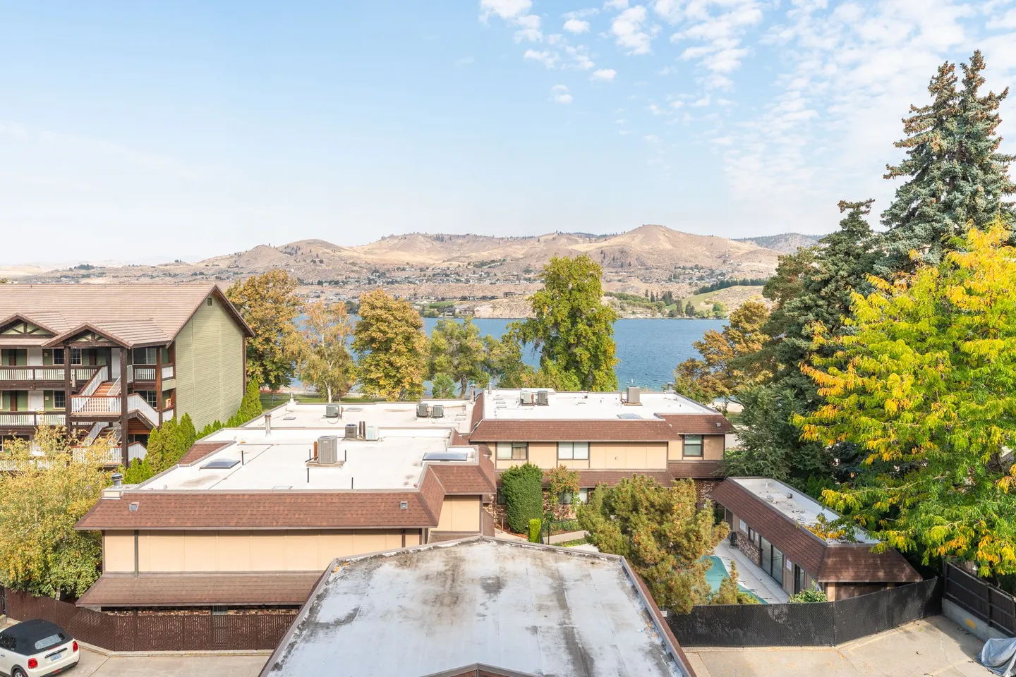 Elevated view overlooking residential buildings toward a blue lake and arid hills under a sunny sky.