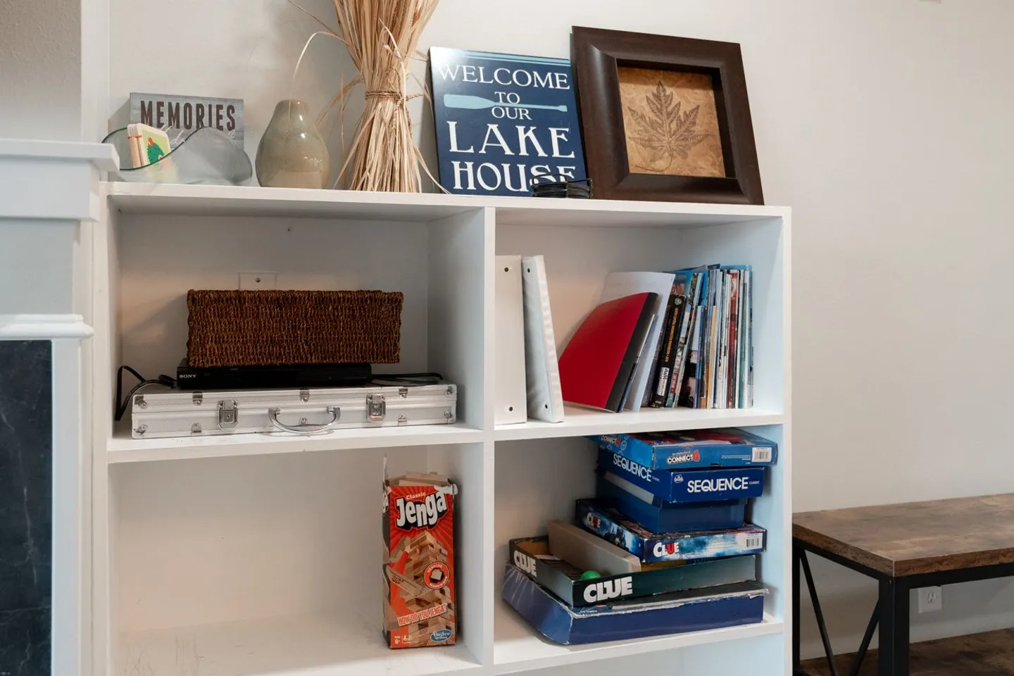 White cubby shelving unit holding board games, media, and decorative items including a Lake House sign.