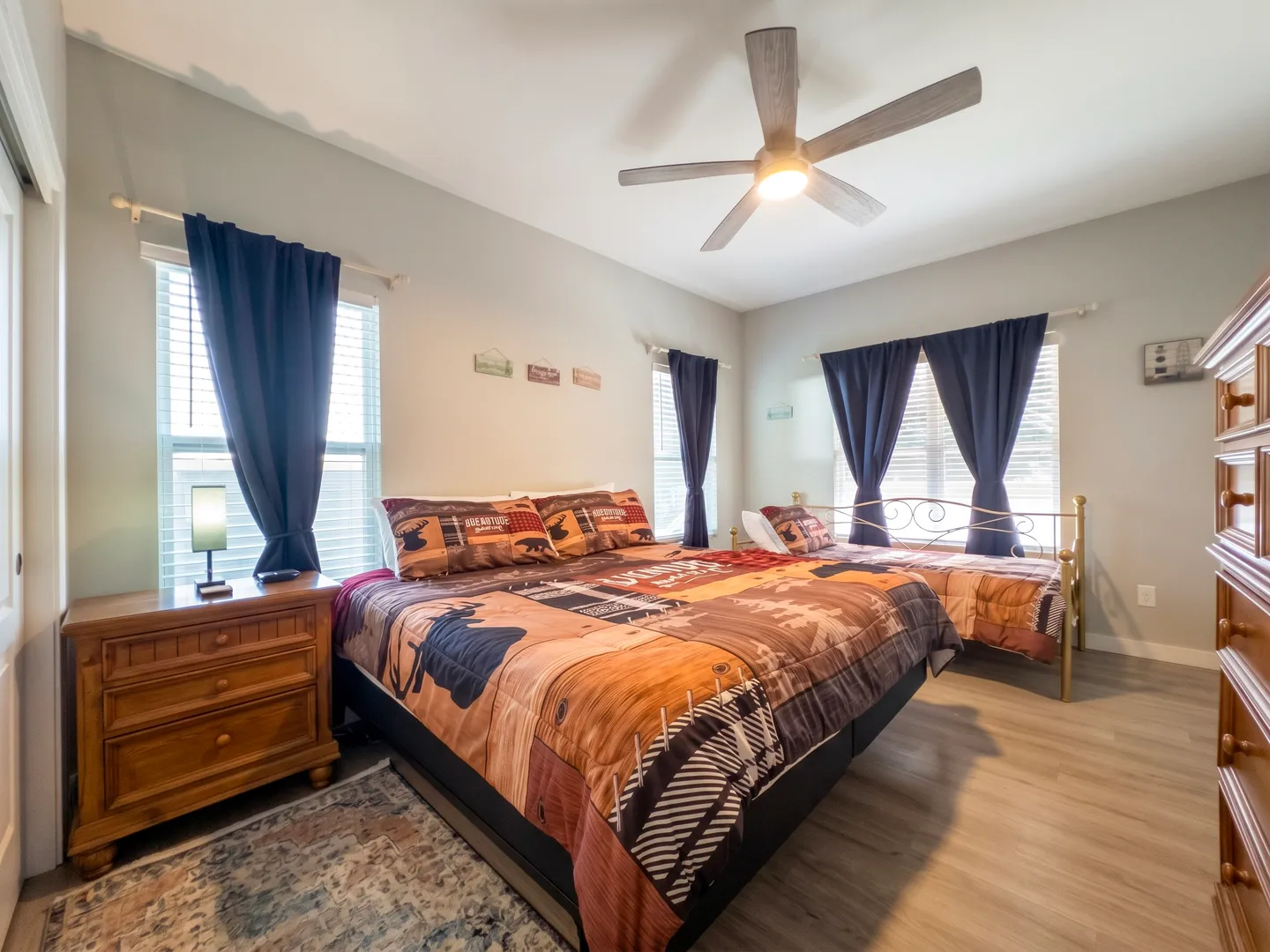 Bedroom featuring two beds with matching rustic wildlife-themed bedding, dark blue curtains, a ceiling fan, and wooden furniture.