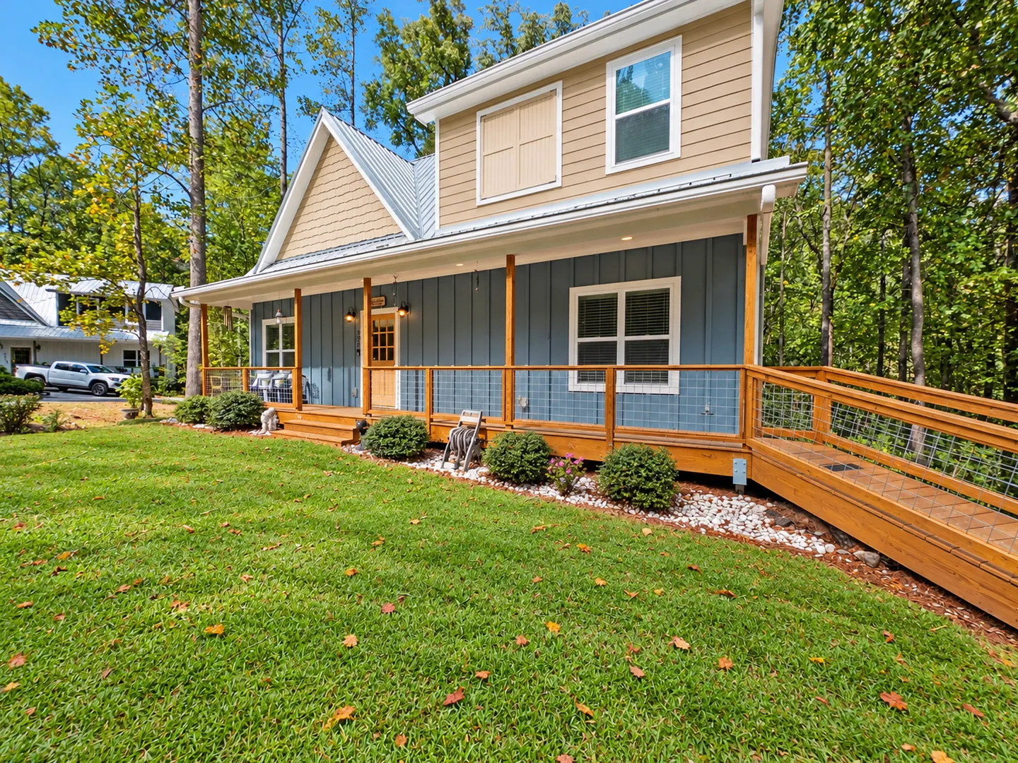Exterior front view of a two-story house with blue and tan siding, a covered front porch with a ramp, and a green front yard surrounded by trees.