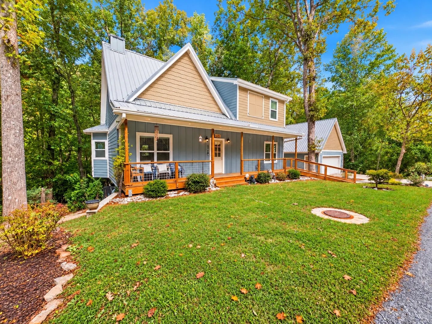 Exterior view of a blue and tan two-story house with a metal roof, front porch, wheelchair ramp, and green lawn.