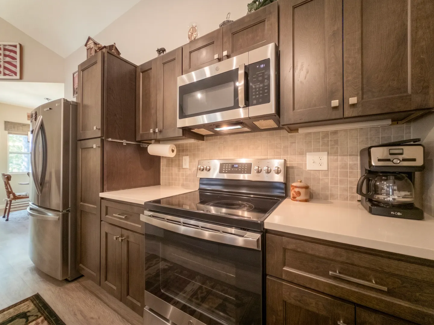 Kitchen counter with dark wood cabinetry, an electric range, over-the-range microwave, and stainless steel refrigerator.