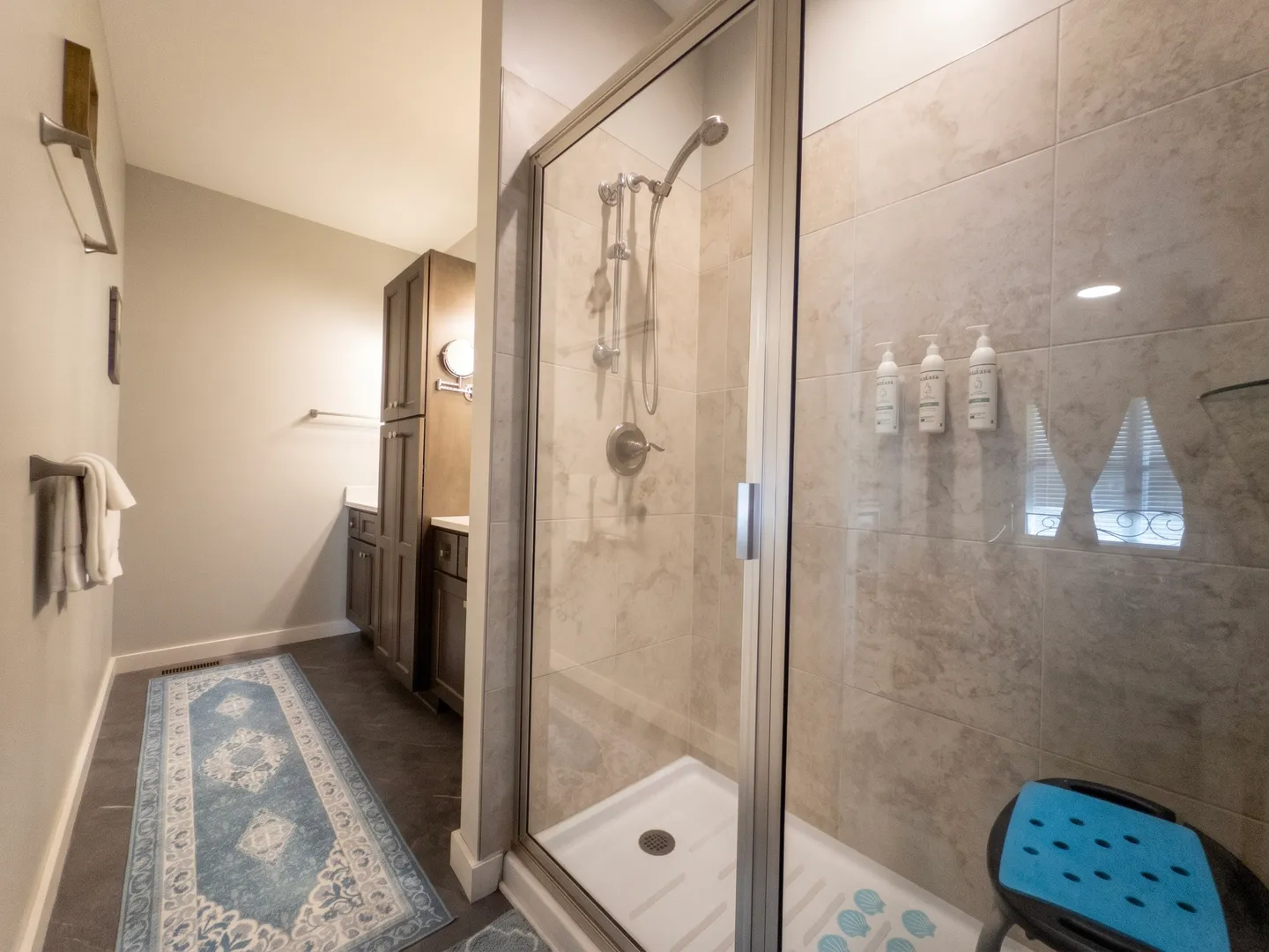 Bathroom showing a glass-enclosed walk-in shower with tiled walls next to a patterned floor runner and dark wood vanity cabinets.