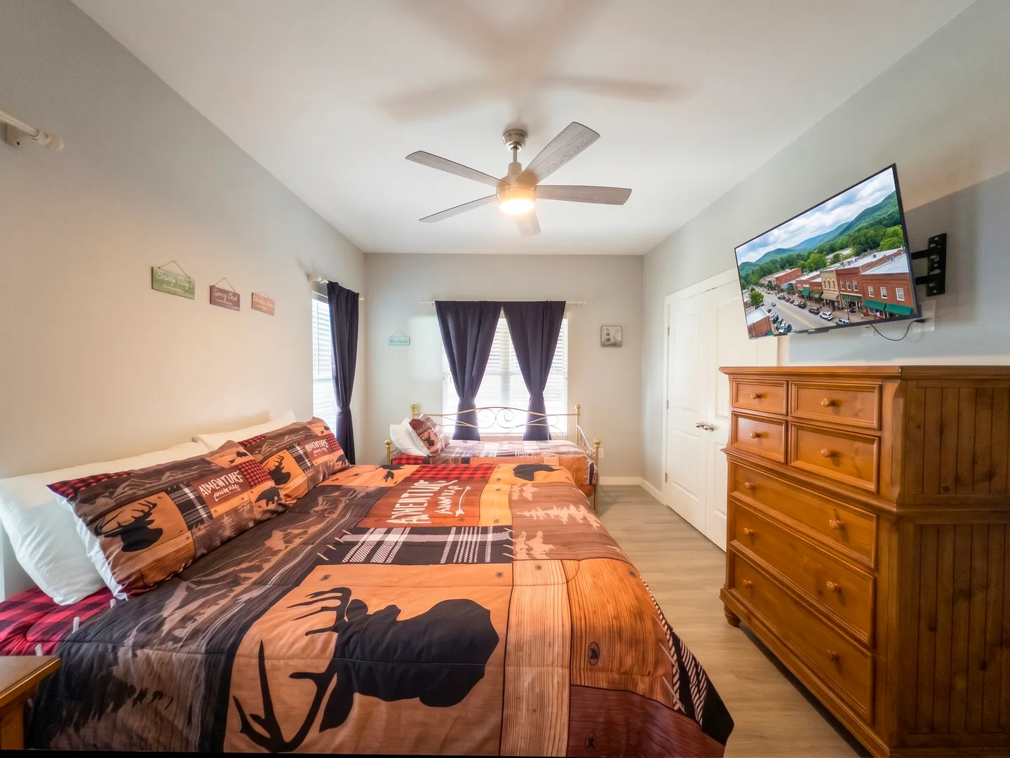 Bedroom with two beds, rustic wildlife bedding, a wooden dresser, ceiling fan, and a wall-mounted television.