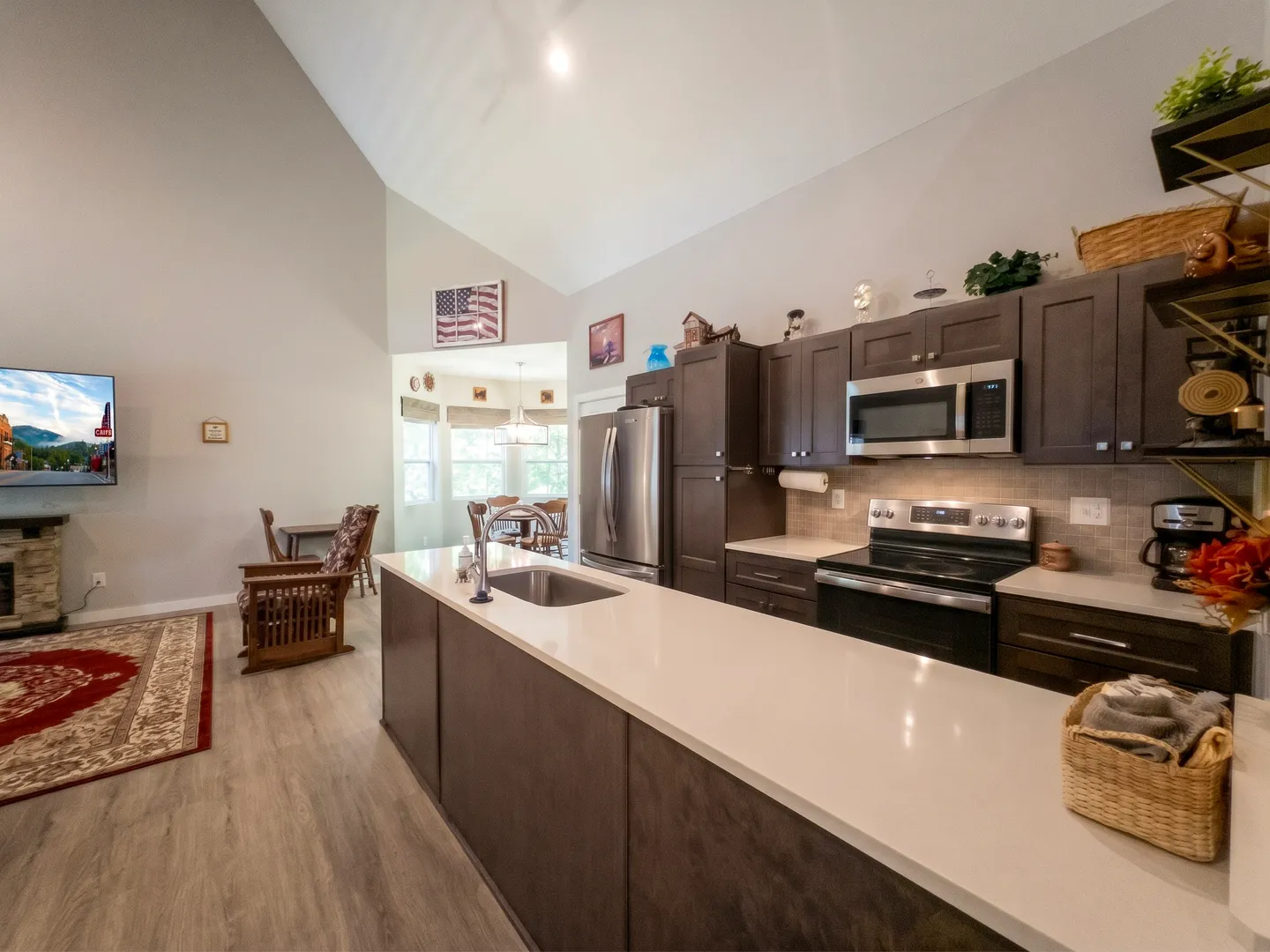 Open-concept kitchen with a large island, dark cabinets, stainless steel appliances, and a vaulted ceiling overlooking the living area.