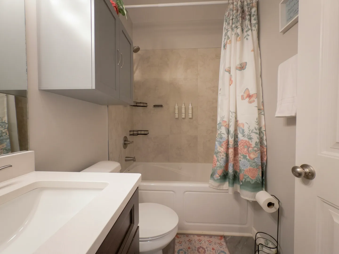 Bathroom with a bathtub and shower combination, floral curtain, toilet, and vanity sink.
