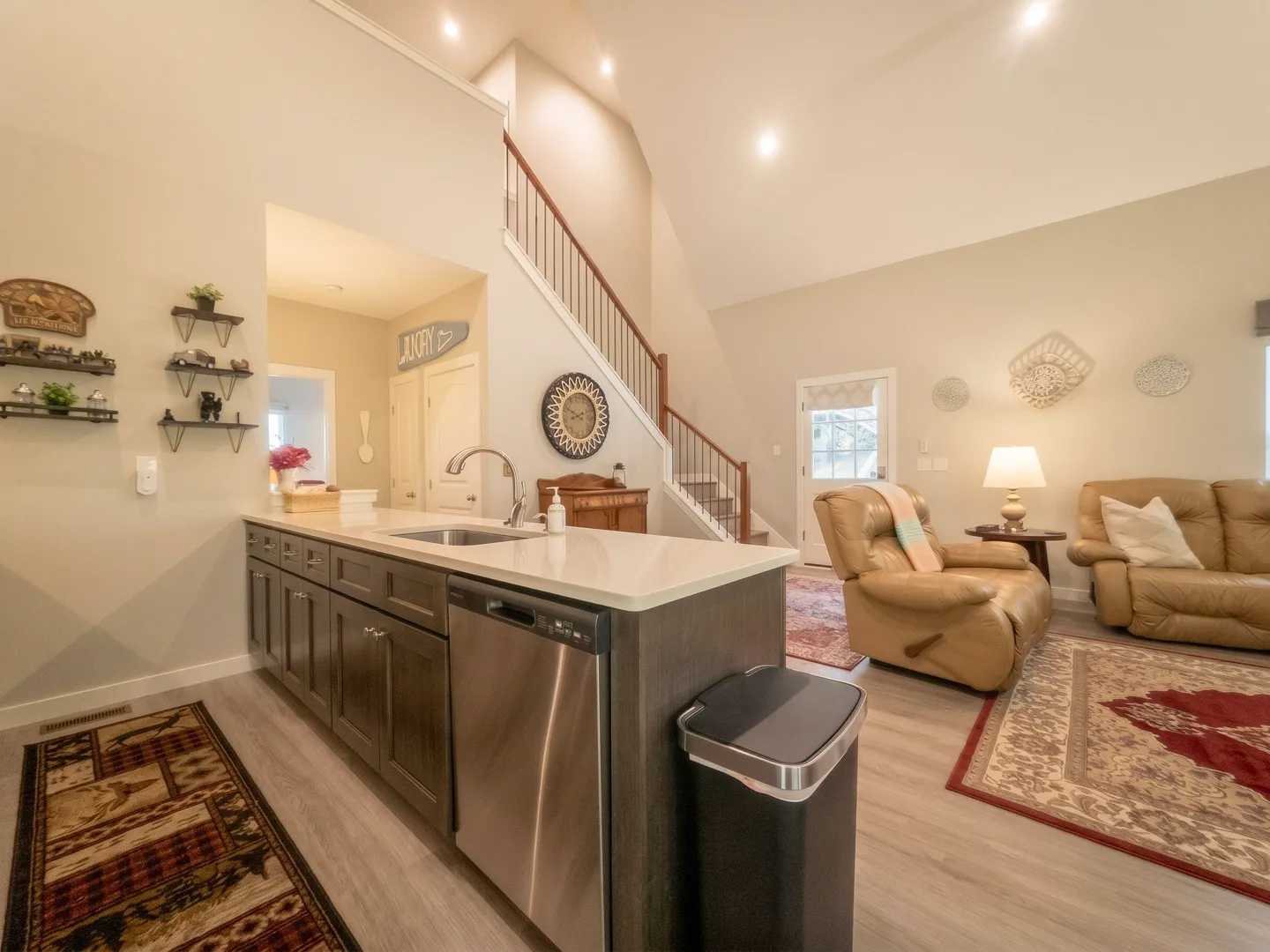Open-concept living room and kitchen counter with stainless steel dishwasher and view of the staircase.