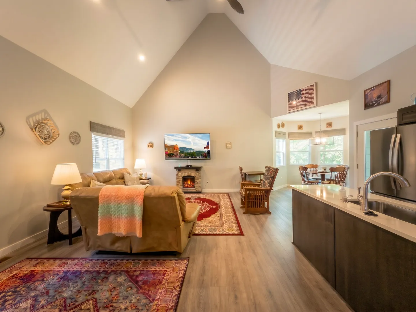 Open-concept living room with vaulted ceiling, leather seating, fireplace, TV, kitchen counter, and adjacent dining area.
