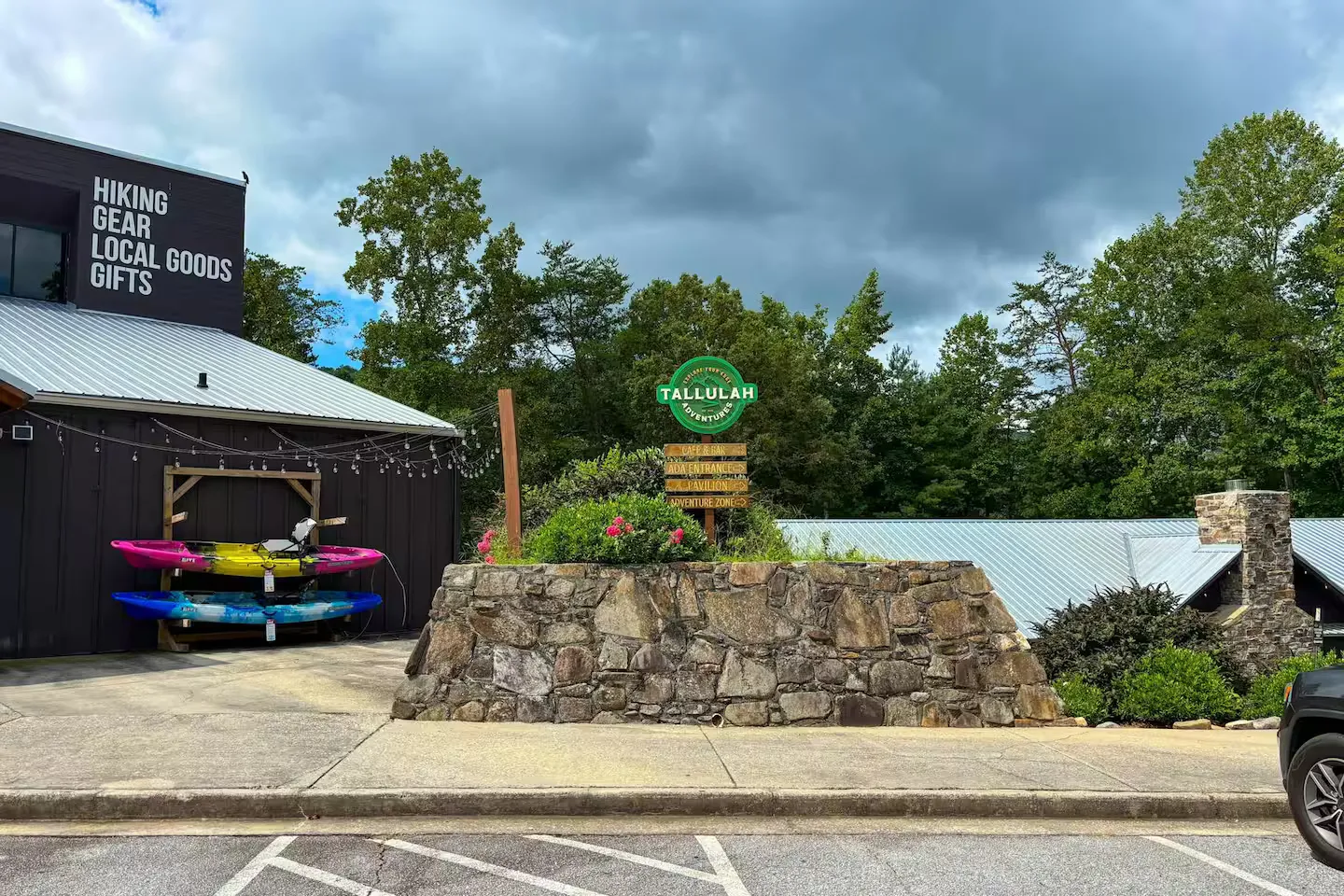 Exterior view of Tallulah Adventures facility featuring a stone retaining wall, colorful kayaks on a rack, and signage.