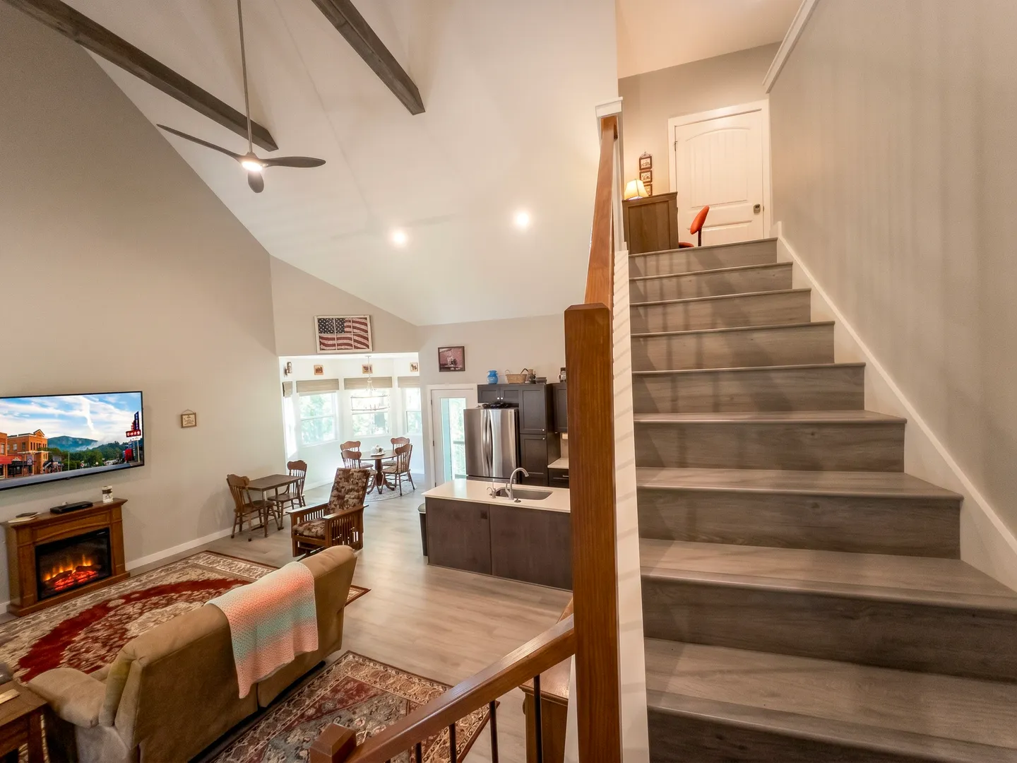 Open-concept living room, kitchen, and dining area viewed from beside a staircase leading to the upper level.