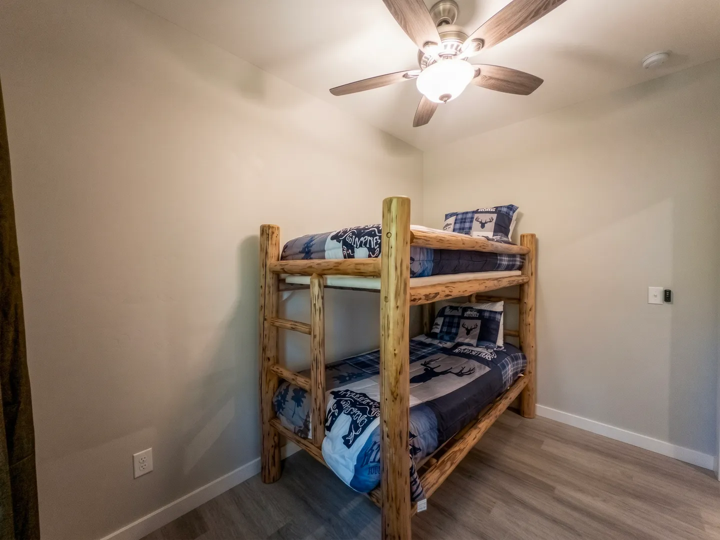 Bedroom corner with rustic log bunk beds and a ceiling fan.