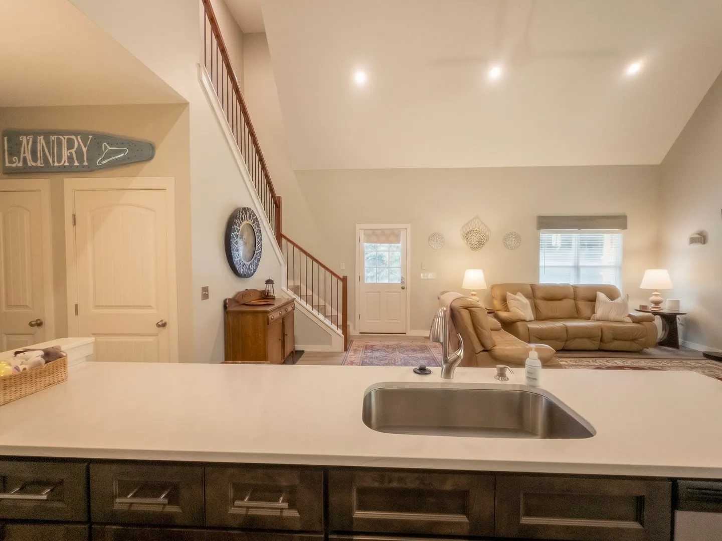 View from kitchen island sink looking into an open-concept living room with vaulted ceilings and staircase.