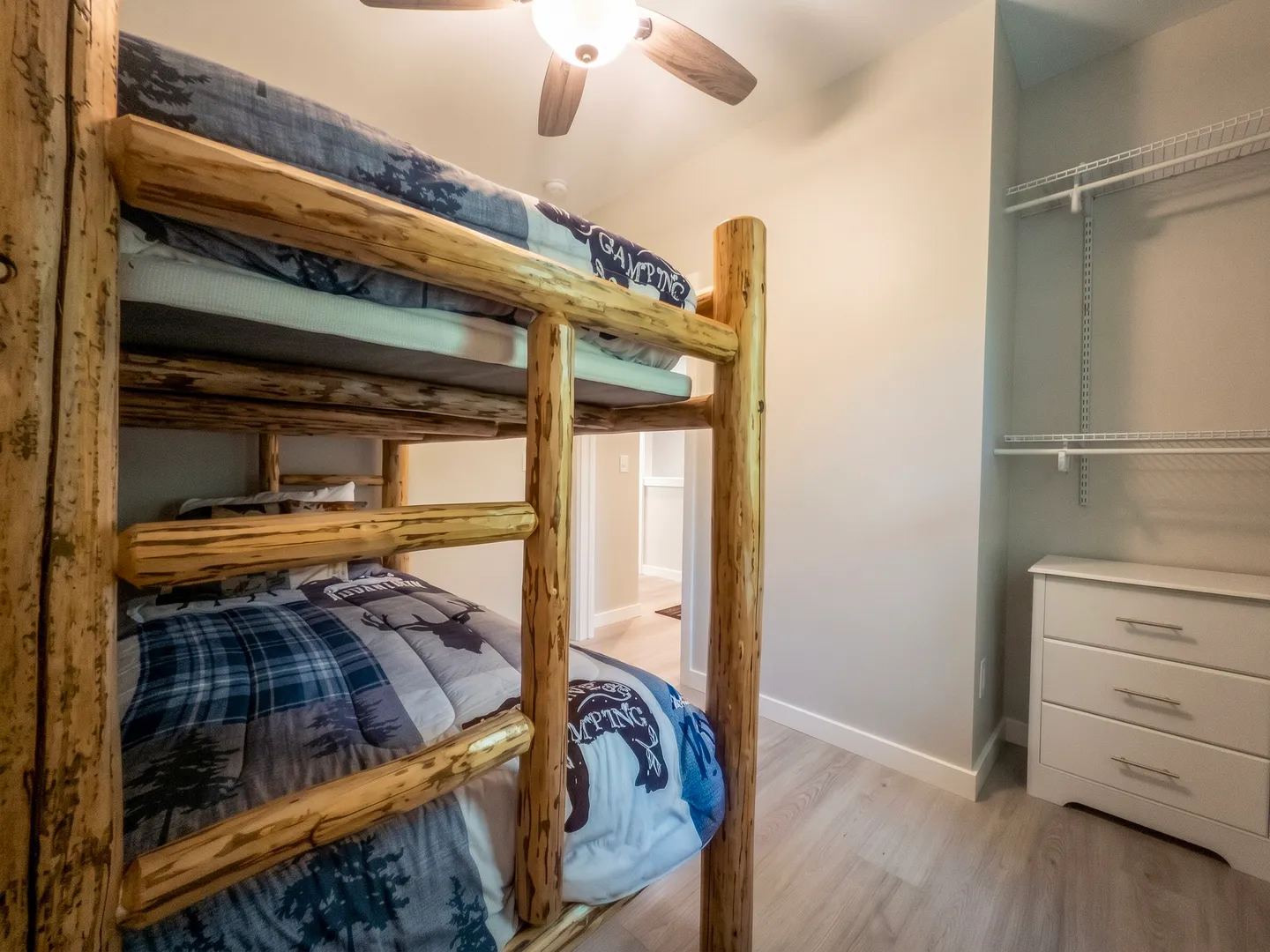 Bedroom featuring a wooden log bunk bed with themed bedding, a ceiling fan, and a closet nook with wire shelving and a white dresser.