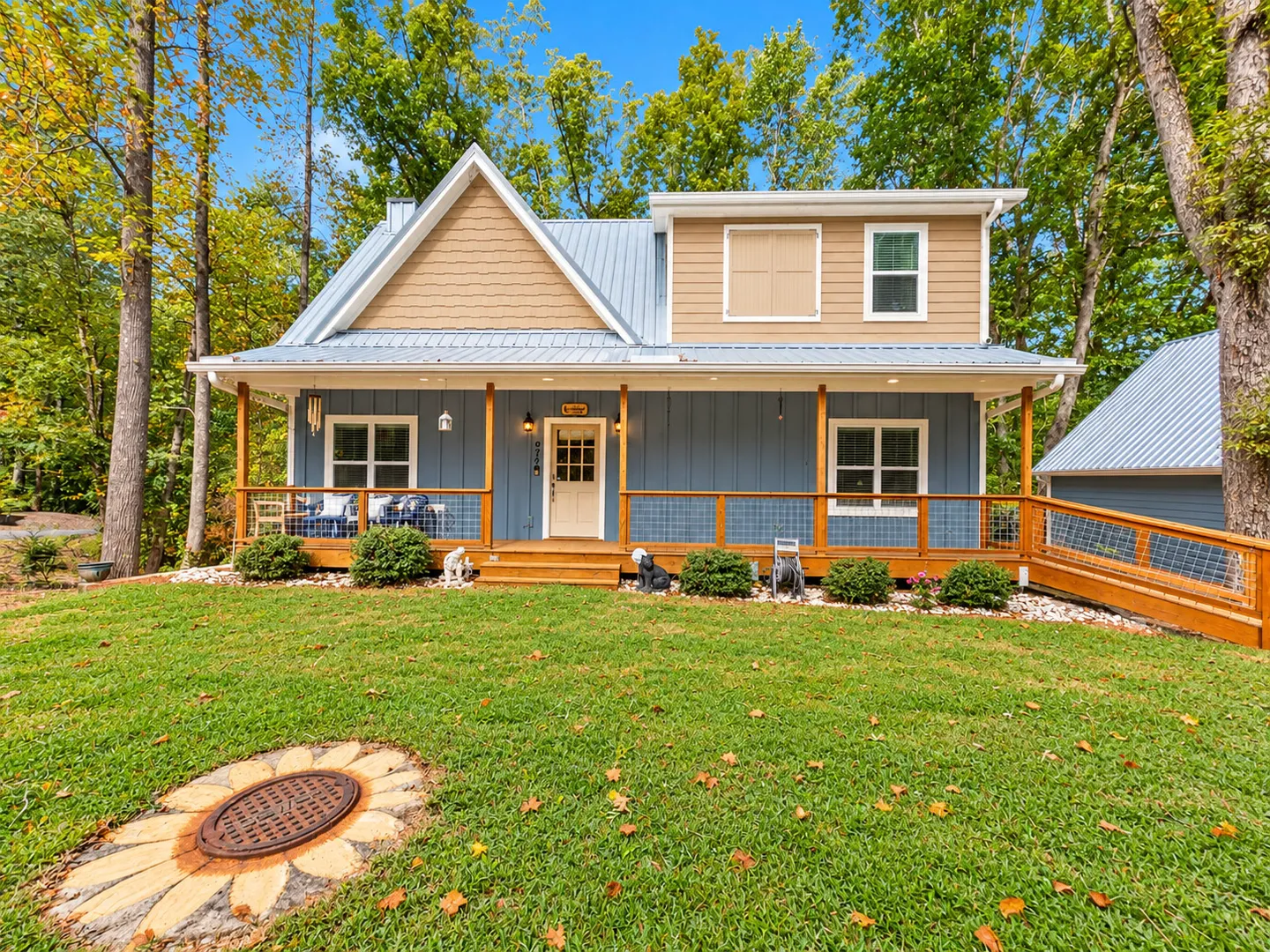 Exterior front view of a two-story home with blue and tan siding, a metal roof, and a covered front porch with a ramp.
