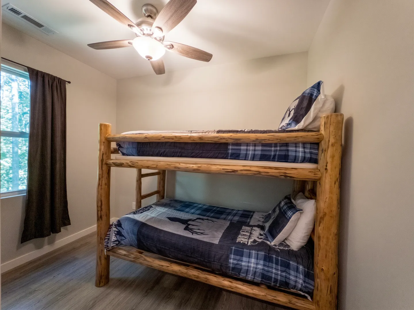 Bedroom featuring a wooden log bunk bed with blue plaid bedding, a ceiling fan with light, and a window with dark curtains.