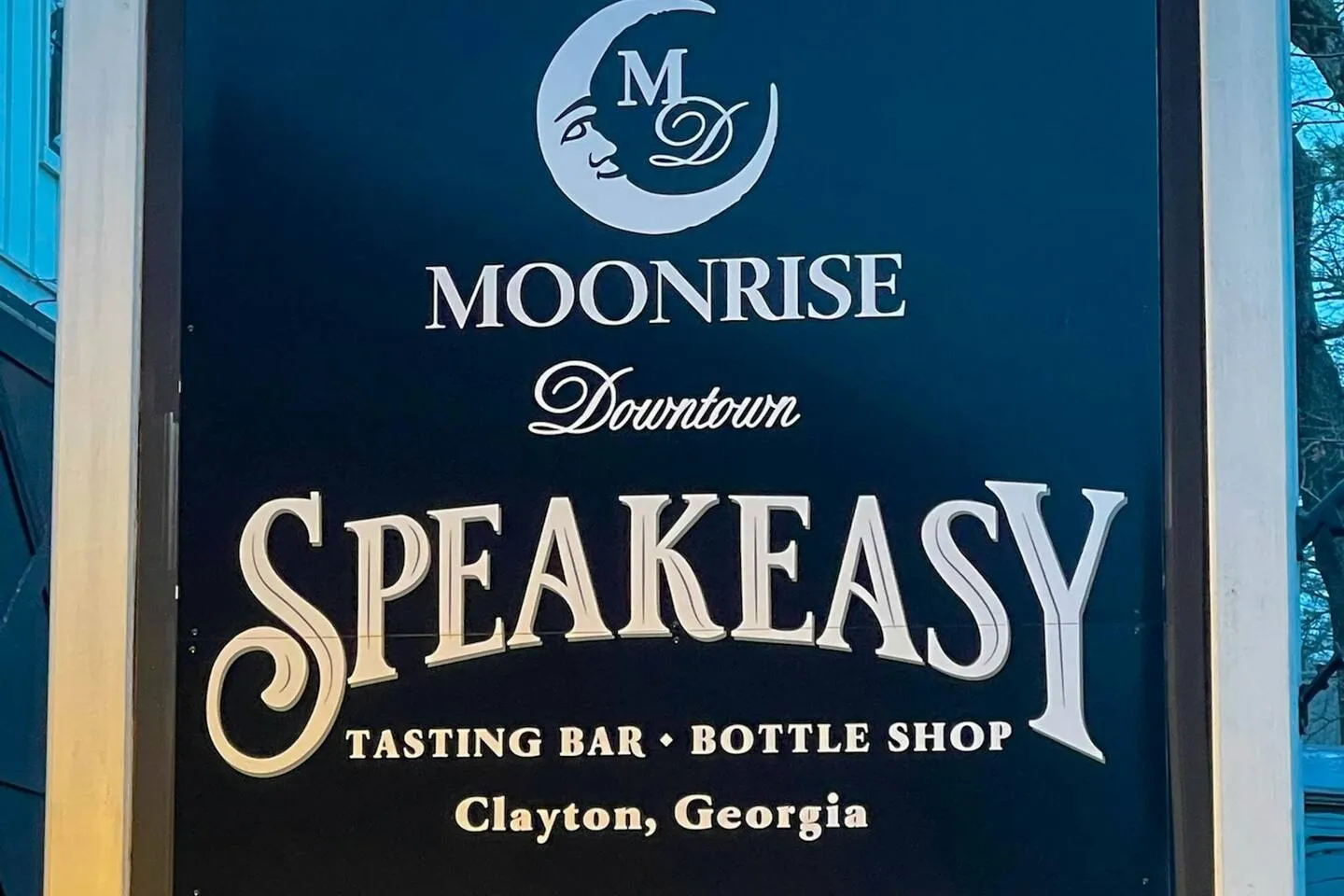 A close-up shot of an outdoor sign for Moonrise Downtown Speakeasy Tasting Bar and Bottle Shop in Clayton, Georgia.