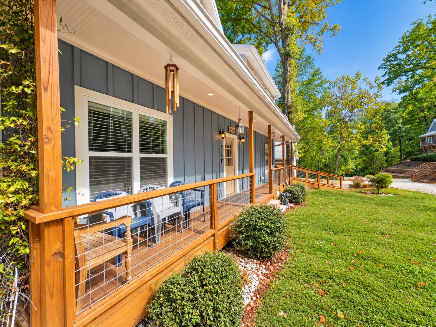 Front porch of a blue home with wooden railings and wire mesh, featuring outdoor seating and an adjoining ramp leading to the yard.