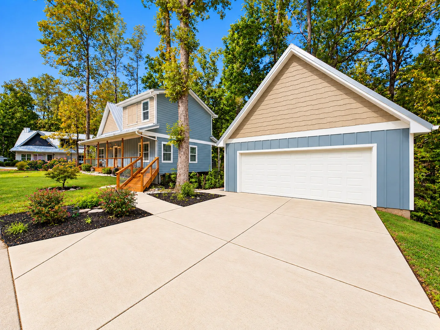 Exterior view of a blue two-story house with a detached garage, concrete driveway, and front lawn surrounded by trees.
