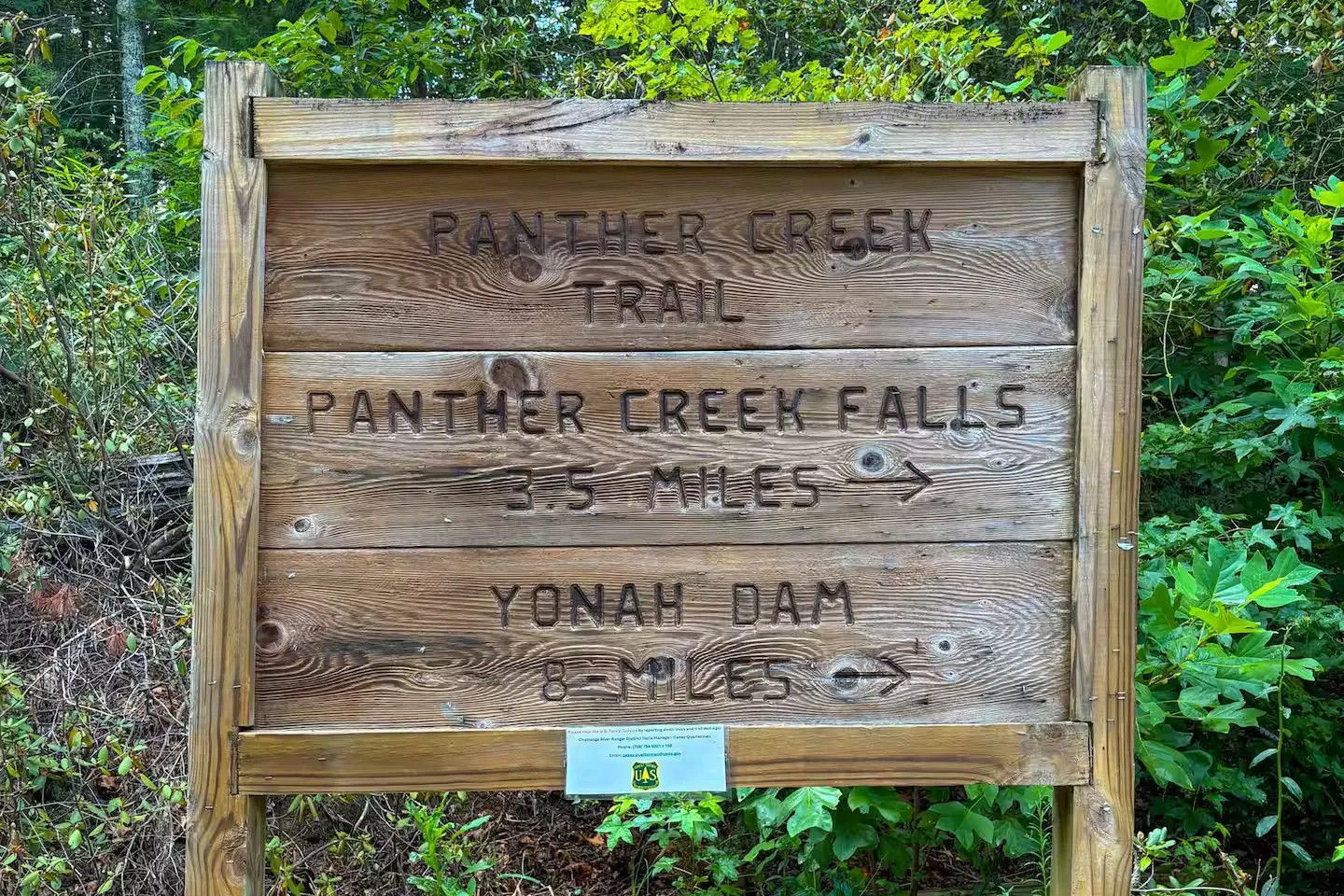 Carved wooden trail sign for Panther Creek Trail indicating distances to Panther Creek Falls and Yonah Dam, surrounded by lush green foliage.