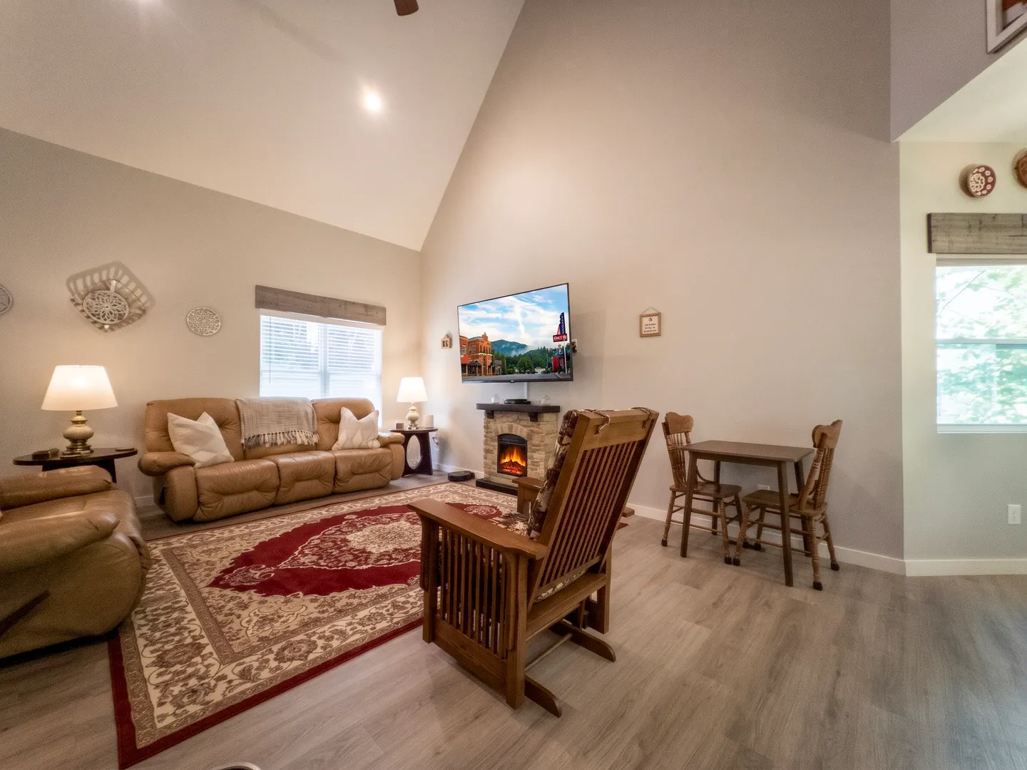 Living room featuring a vaulted ceiling, leather seating, a wall-mounted TV over an electric fireplace, and a small dining table.