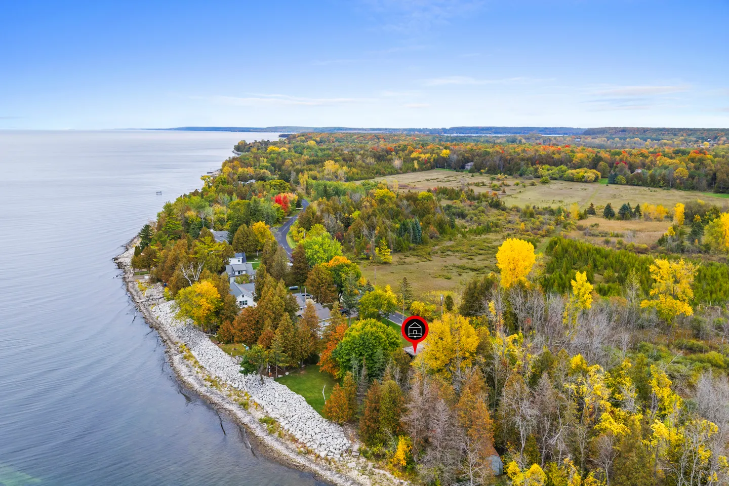 Aerial view of a coastal peninsula with houses tucked among autumn trees along a rocky shoreline and large body of water.