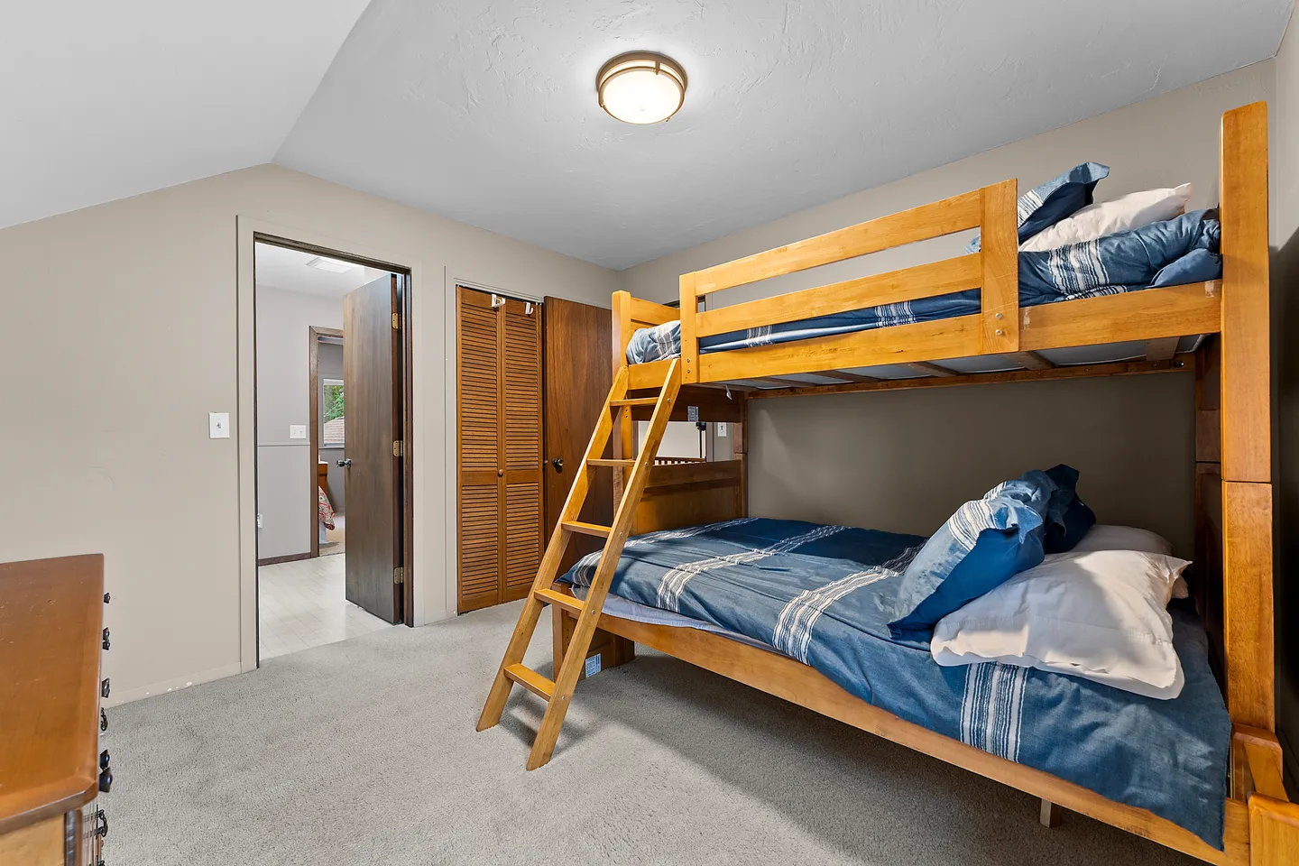 Bedroom featuring a wooden bunk bed with blue bedding, beige walls, carpeted floor, and closet with louvered doors.