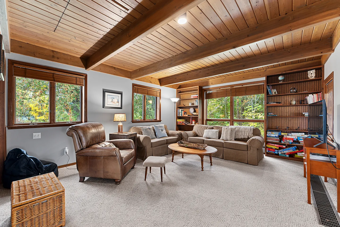 Living room with carpeted floor, wood-paneled ceiling with exposed beams, sofas, leather armchair, and built-in bookshelves.