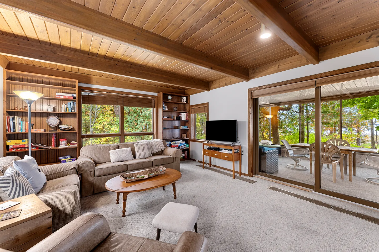 Living room featuring a wood-paneled ceiling with exposed beams, carpeted floor, sofa seating, and large sliding glass doors leading to an outdoor deck.
