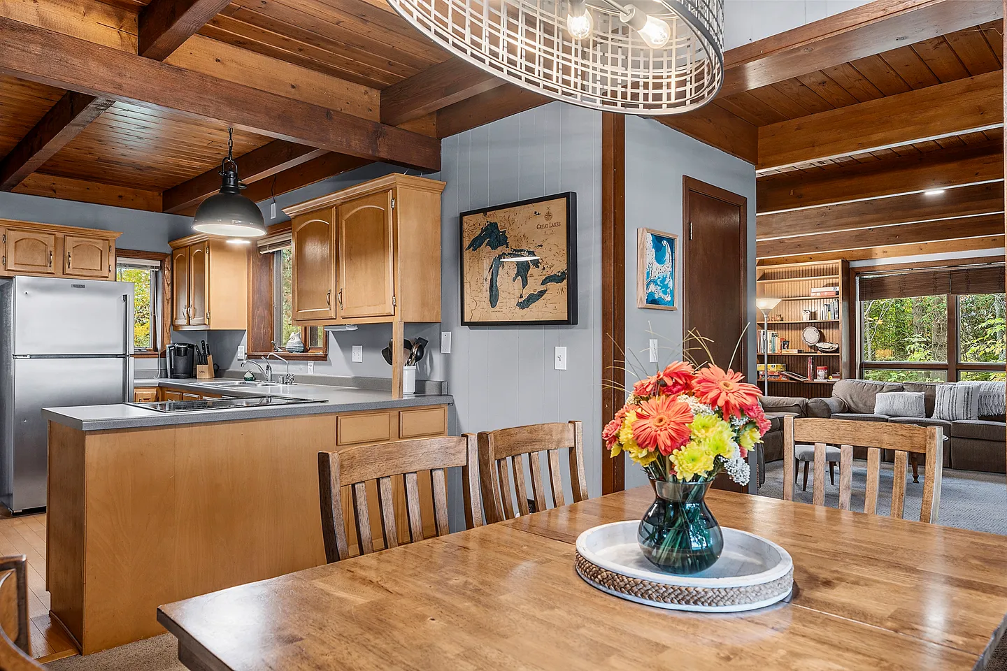 Dining area with a wooden table looking towards an open kitchen and adjacent living room with wood beam ceilings.