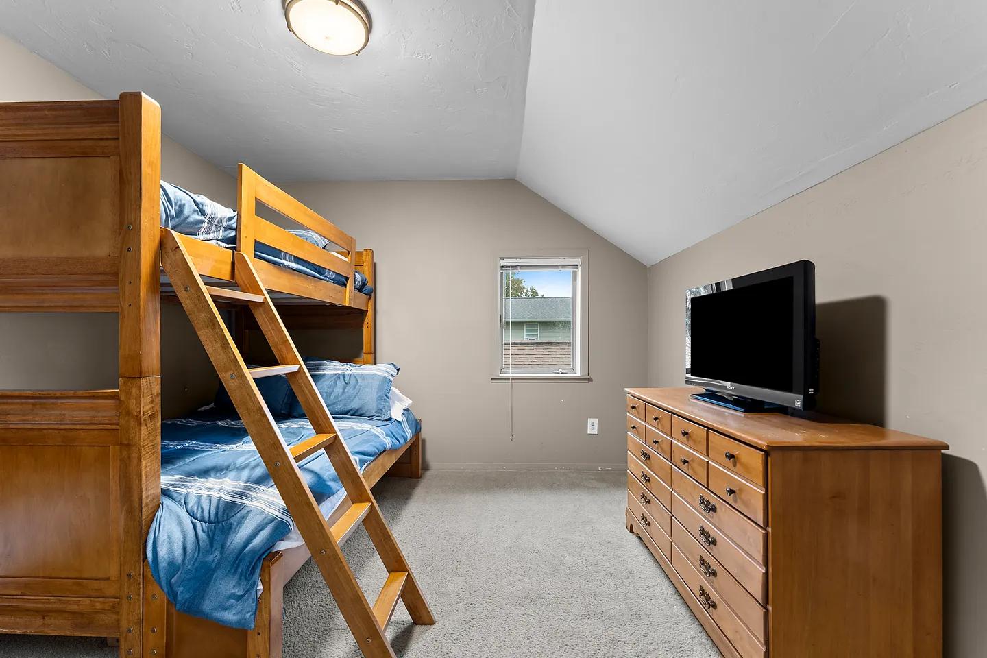 Bedroom with wooden bunk beds, a matching dresser with a television, carpeted flooring, and an angled ceiling.