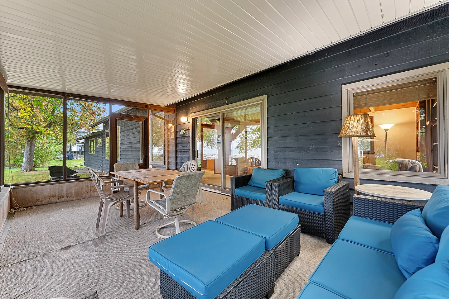 Screened porch furnished with bright blue outdoor seating, a small dining table, and dark horizontal siding along the house wall.