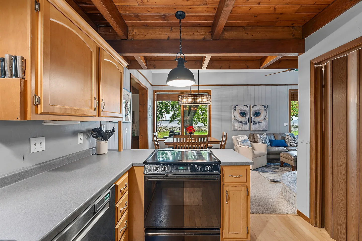 Kitchen counter and stove looking into an open dining area and living room with exposed wood beam ceiling.