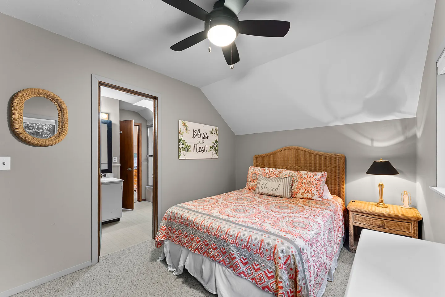 Bedroom with patterned bedding, wicker headboard, ceiling fan, and open doorway leading to an en-suite bathroom.