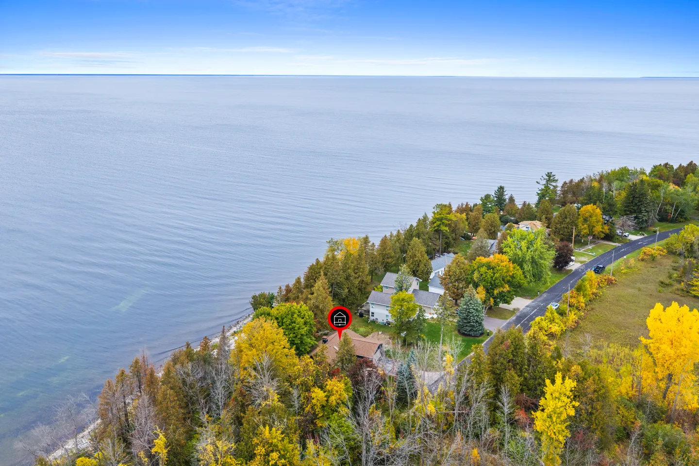 Aerial view of a home nestled among colorful autumn trees on the edge of a vast body of water.