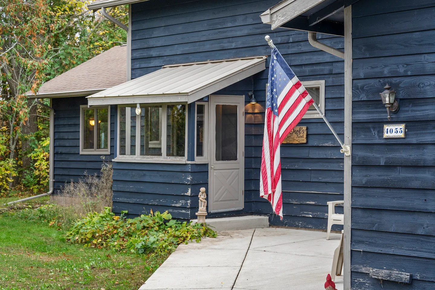 Exterior entrance of a blue home with a metal awning over the doorway and an American flag mounted on the wall.