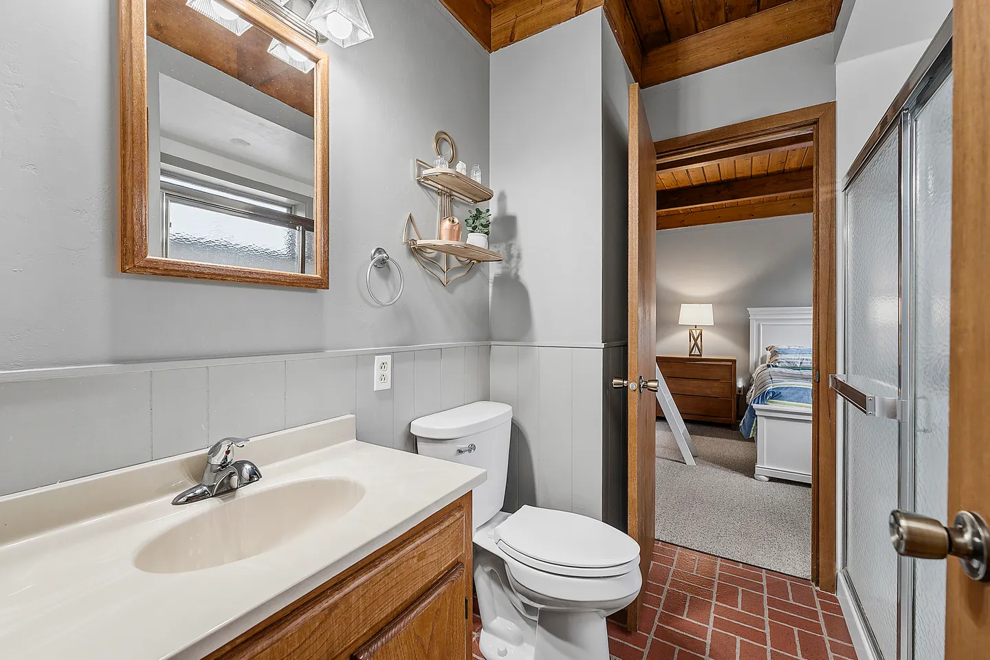 Bathroom with a wood vanity, white toilet, walk-in shower with sliding door, and an open doorway leading to a bedroom.