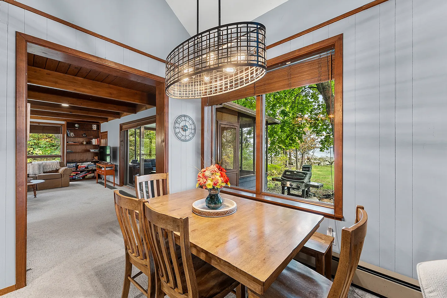 Dining area with a wooden table, matching chairs, and a modern wireframe chandelier next to large picture windows looking outside.
