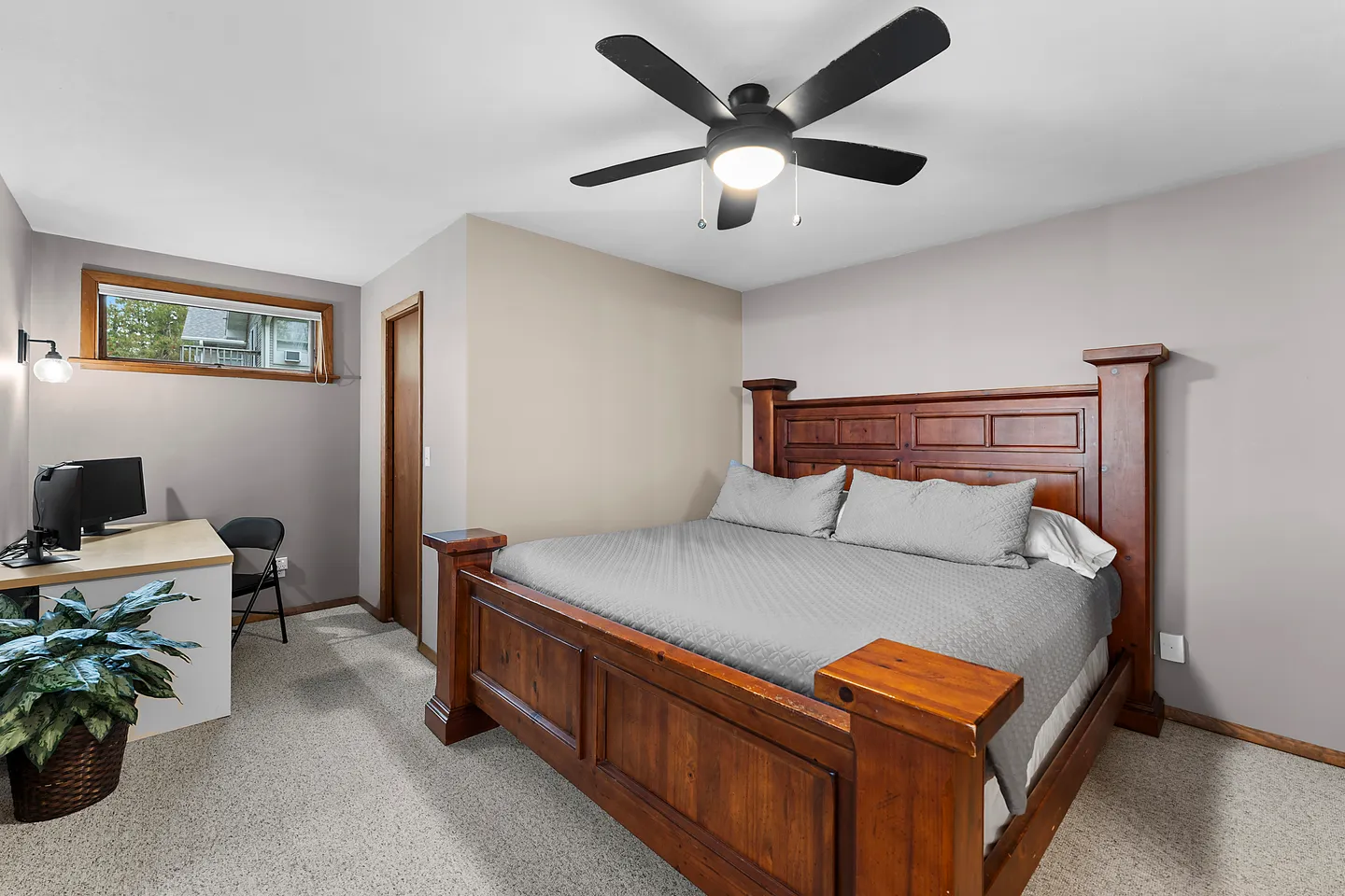 Bedroom featuring a wooden bed frame, ceiling fan, carpeted floor, and a work desk with a computer monitor.