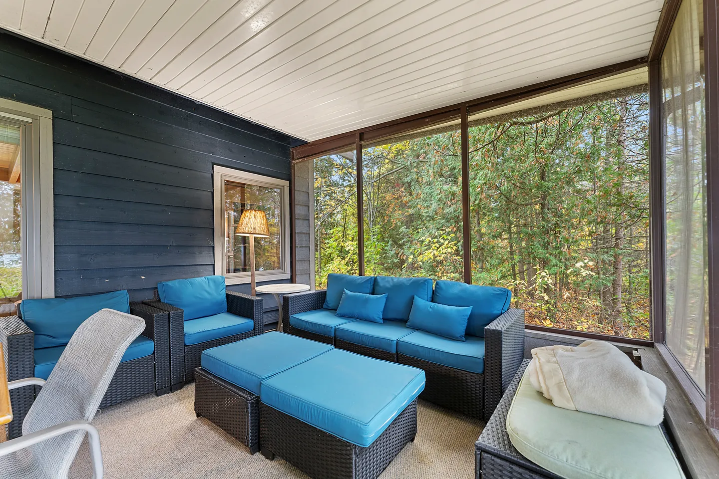 Screened porch furnished with woven outdoor seating featuring bright turquoise cushions, overlooking surrounding trees.