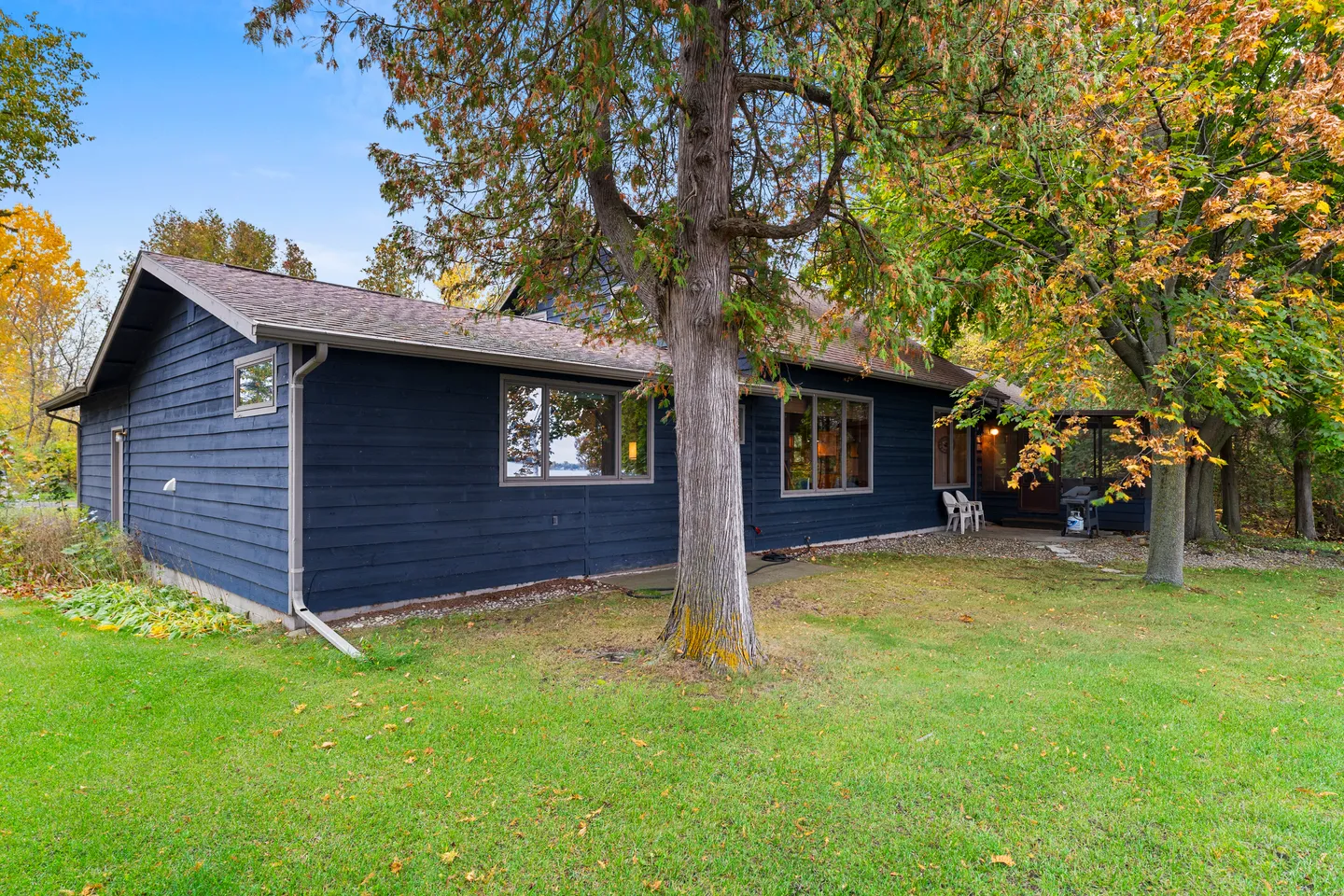 Exterior view of a dark blue one-story house with a green lawn and mature trees in the yard.
