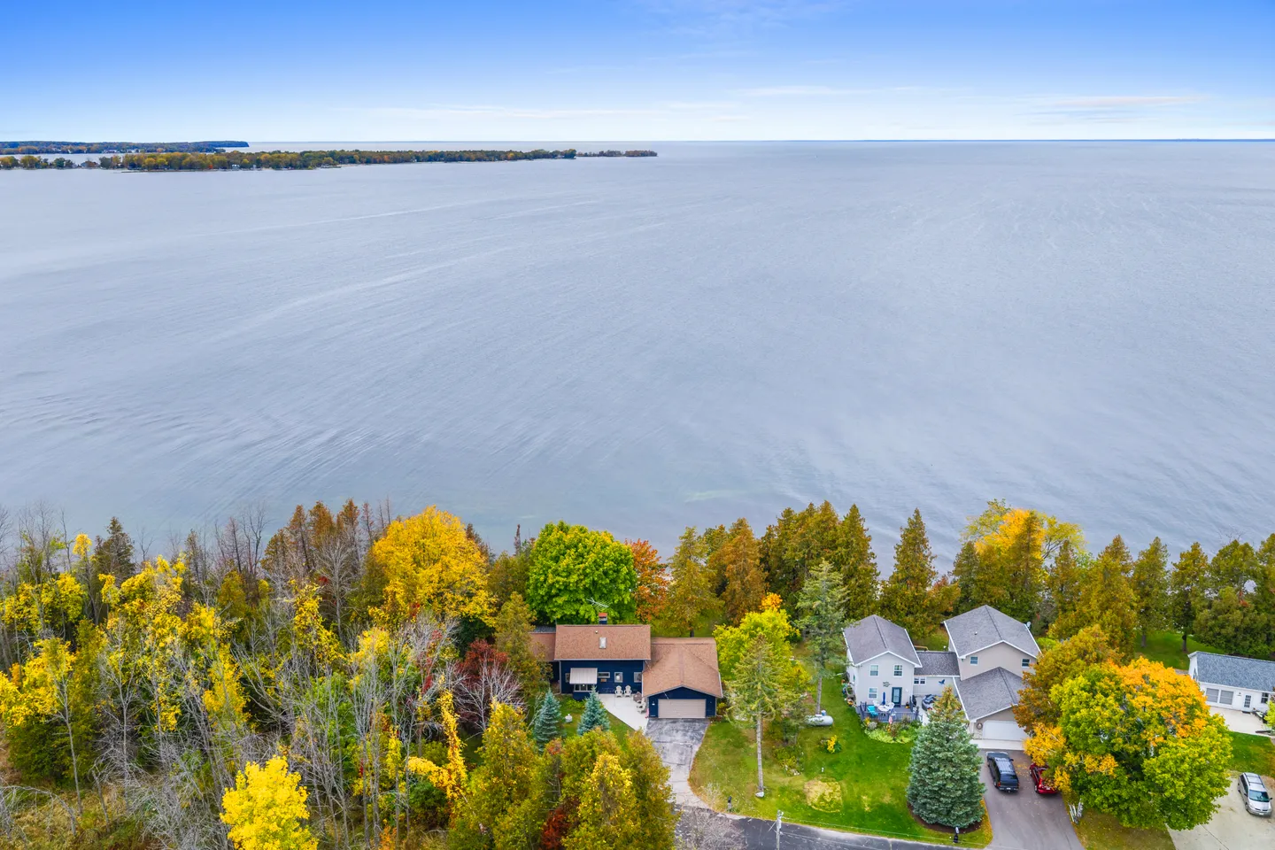 Aerial view of a waterfront home nestled among colorful autumn trees on the shoreline of a vast lake or bay.