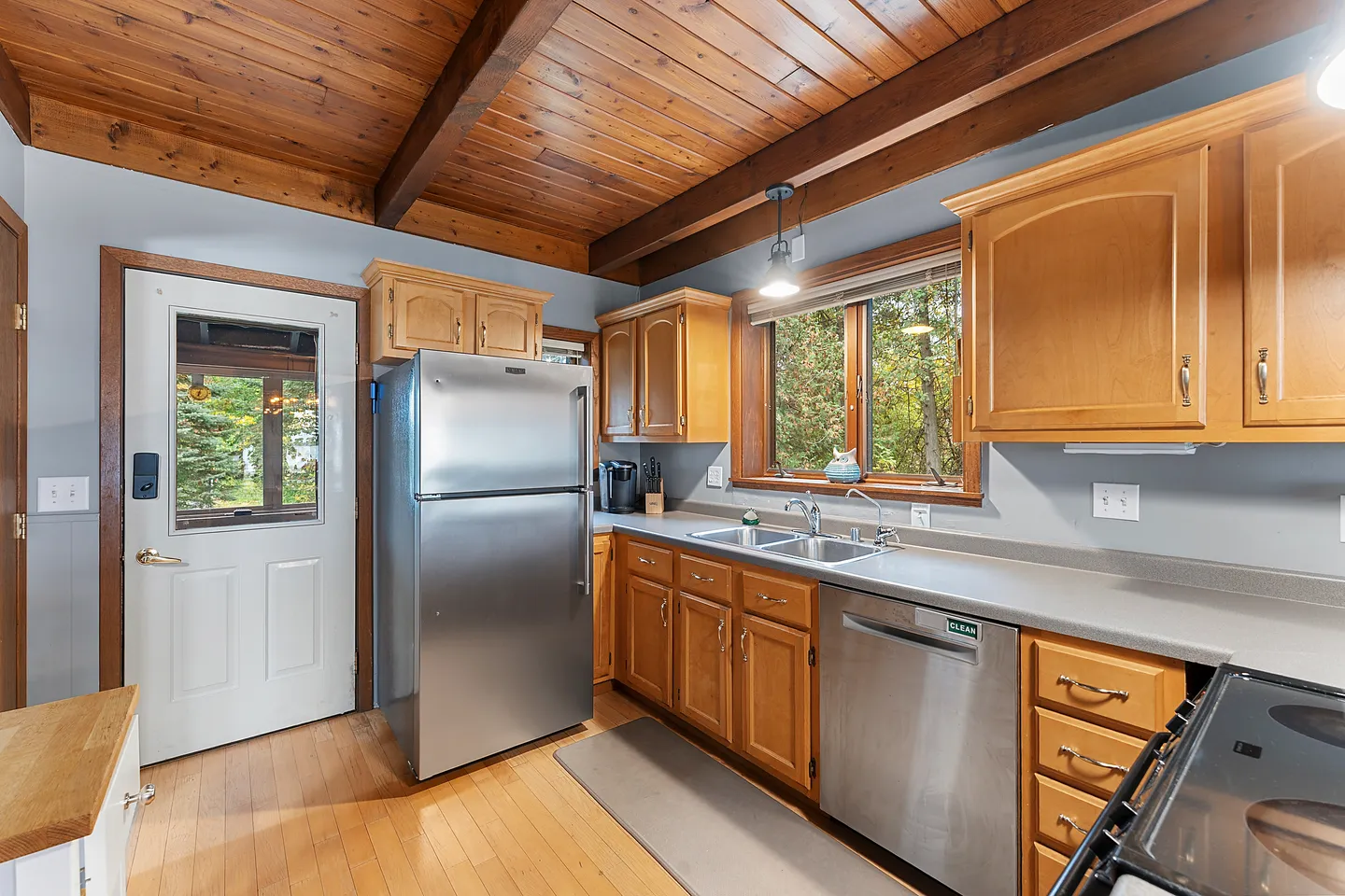 Kitchen with stainless steel appliances, wooden cabinets, wood-paneled ceiling, and an exterior door with a glass window.