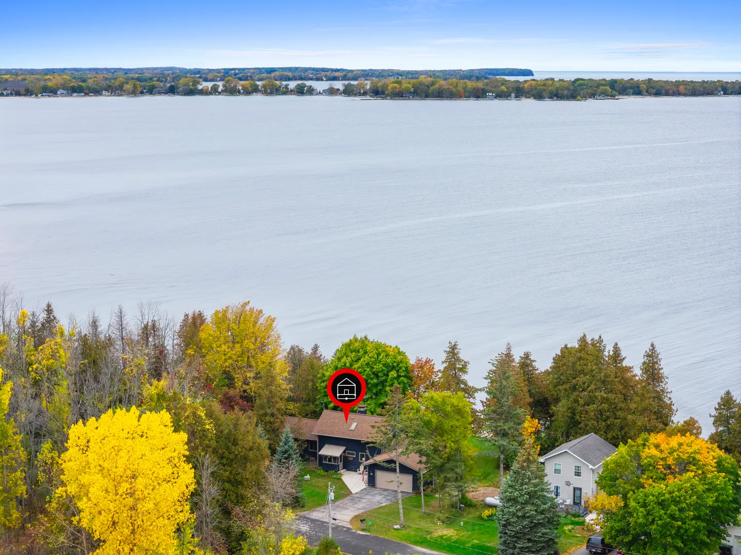 Aerial view of a home along a large body of water surrounded by autumn trees.