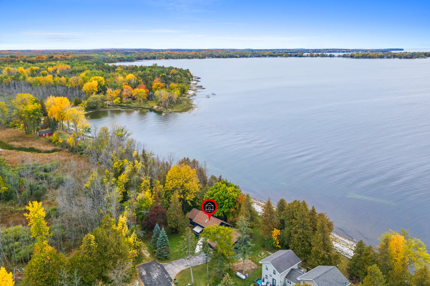 Aerial view of a wooded shoreline on a large body of water with a home marked by a red icon.