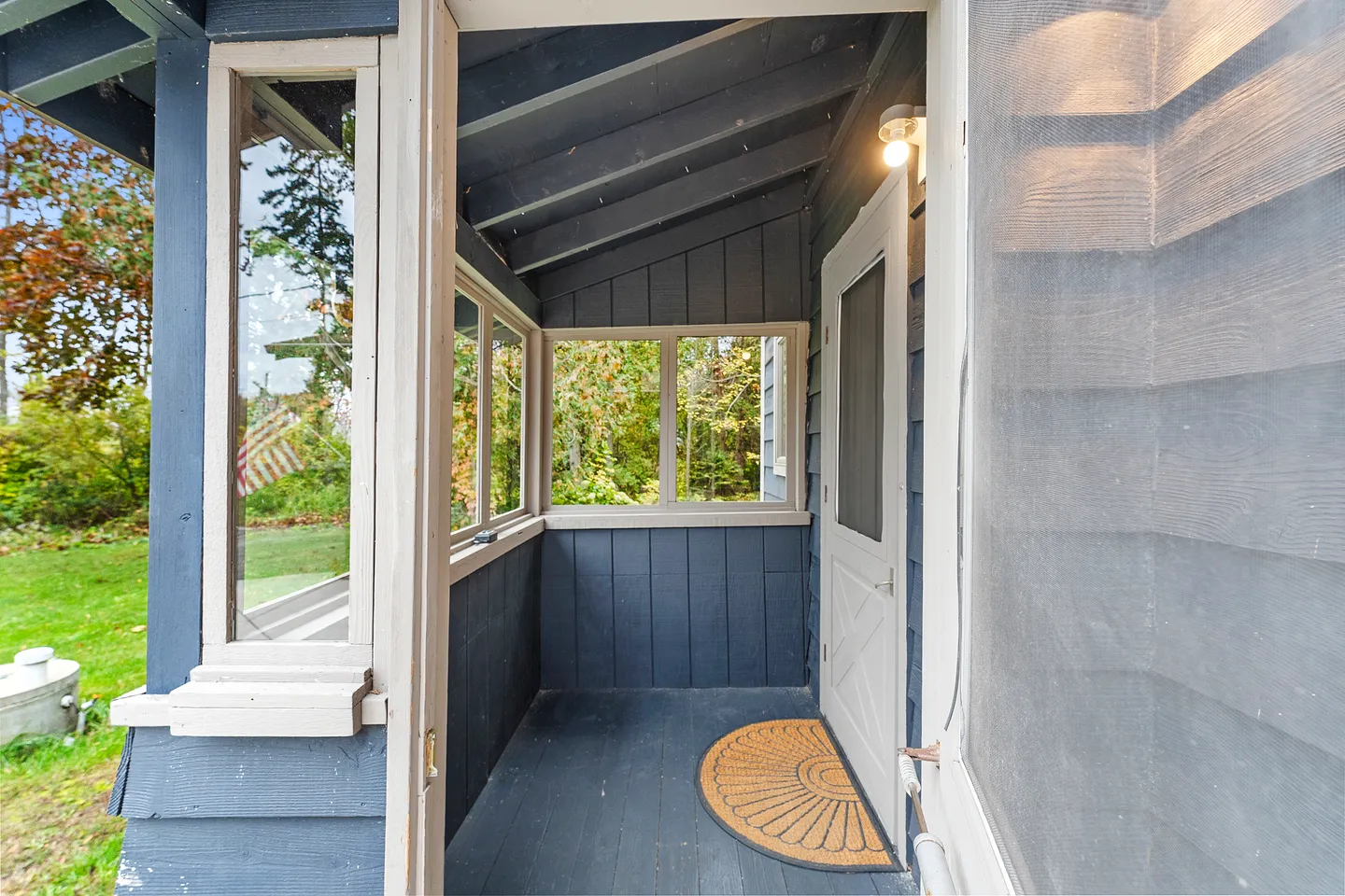 Enclosed blue entryway porch with windows, angled ceiling rafters, and a front entry door with a screen door.