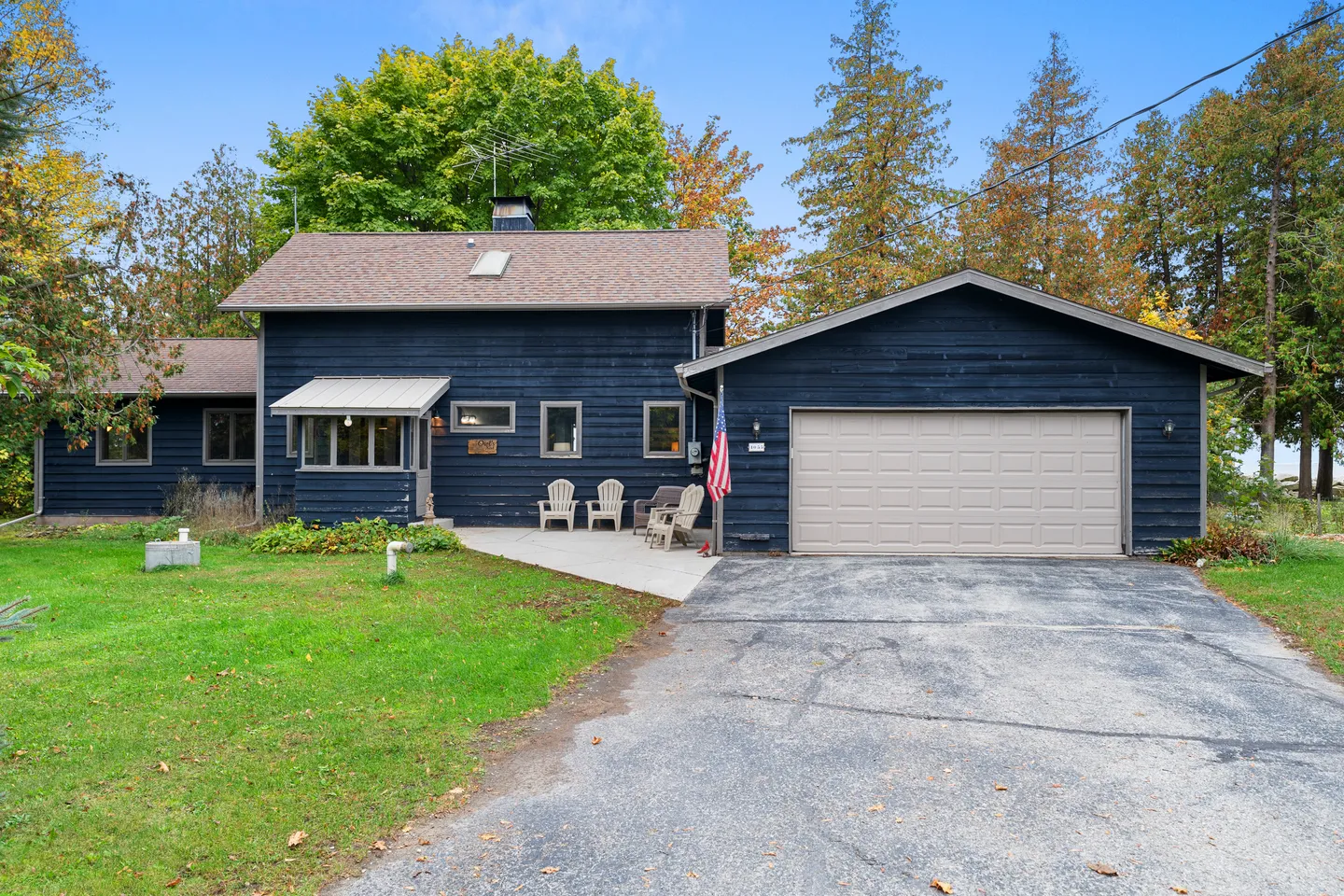 Exterior view of a dark blue, two-story house with an attached garage, paved driveway, and front seating area surrounded by trees.