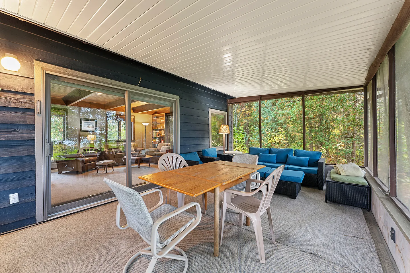 Screened porch with dining table and chairs, outdoor sofa with bright blue cushions, and sliding glass doors to the living room.