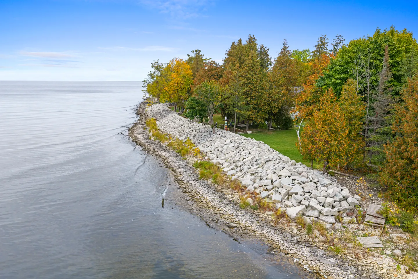Aerial view of a rocky shoreline with large boulders separating a grassy wooded yard from the calm water.