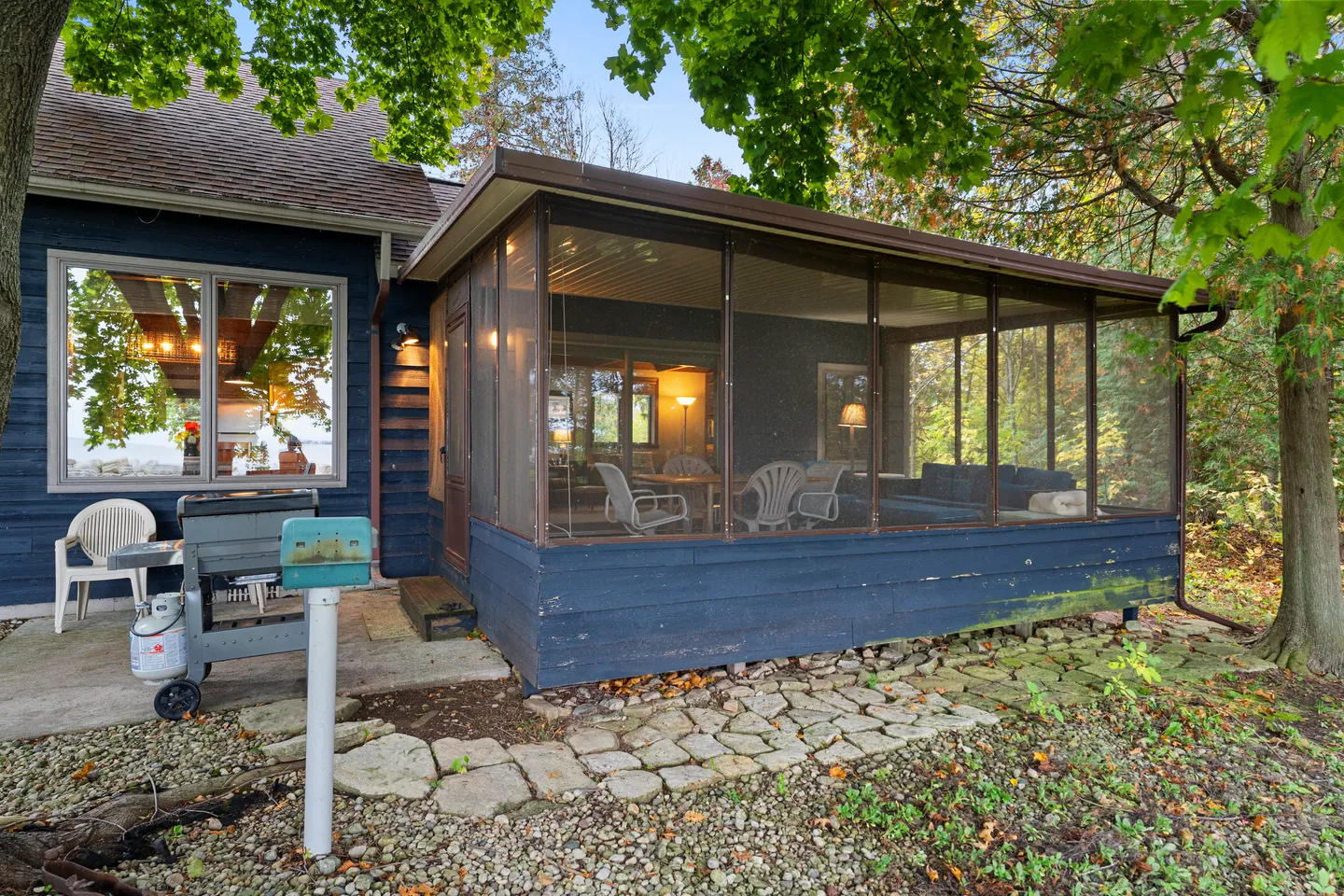 Exterior view of a dark blue house with a screened porch, stone path, and outdoor grill.